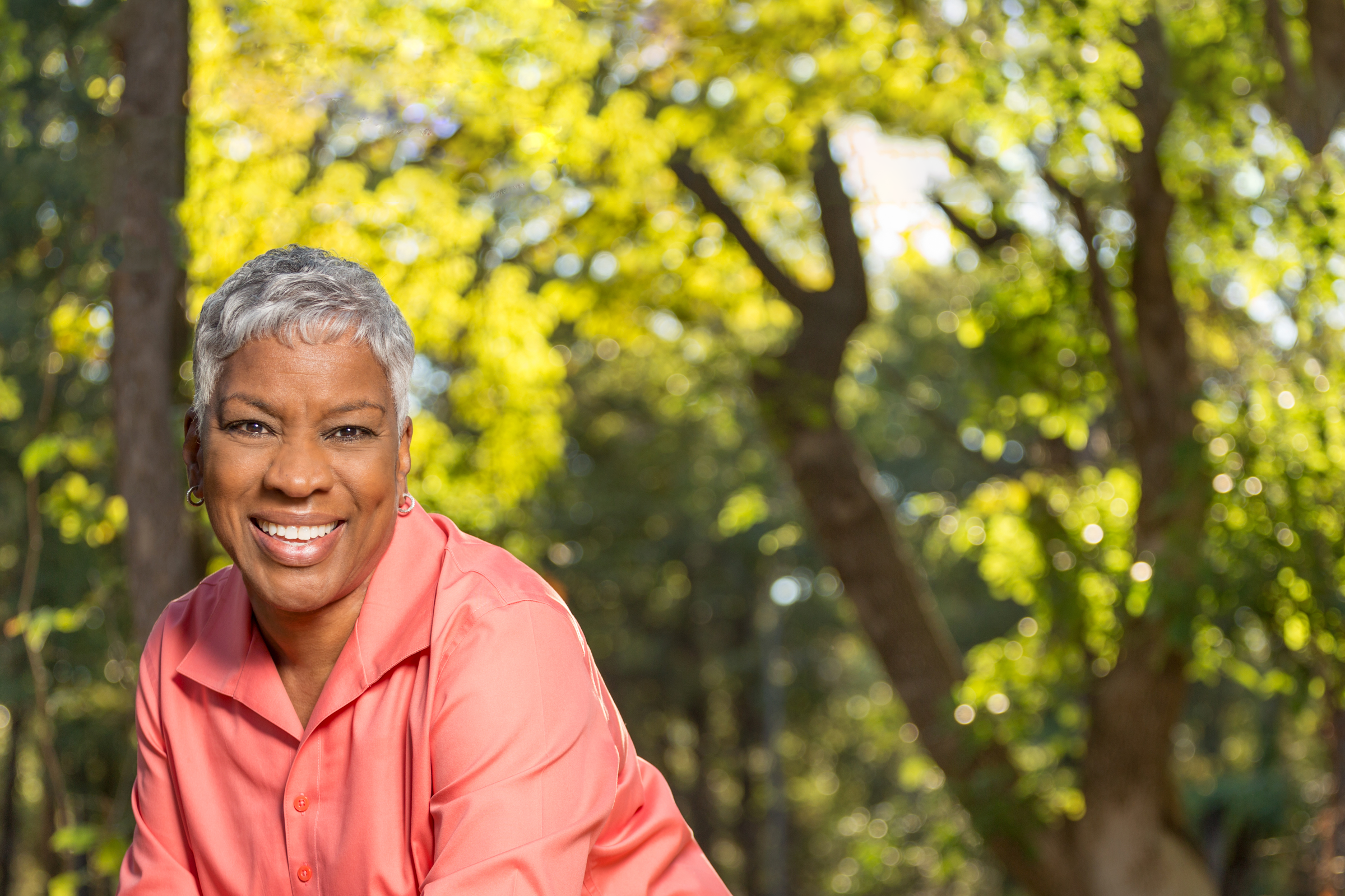 A woman is shown in front of trees.